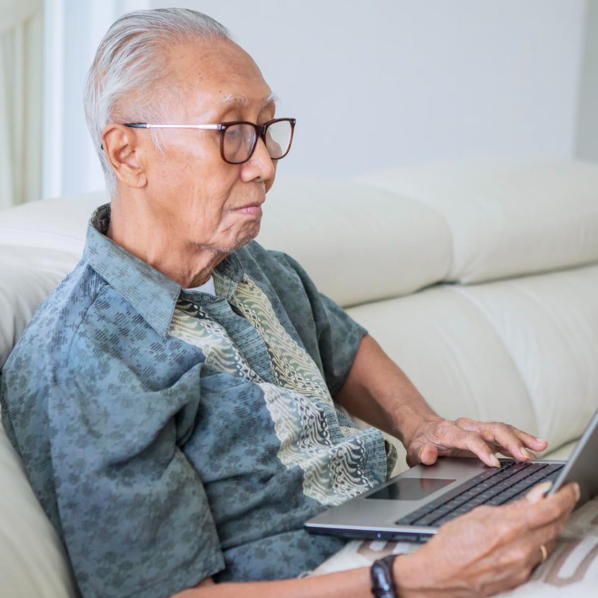 Gray haired man sitting on the couch looking at his laptop