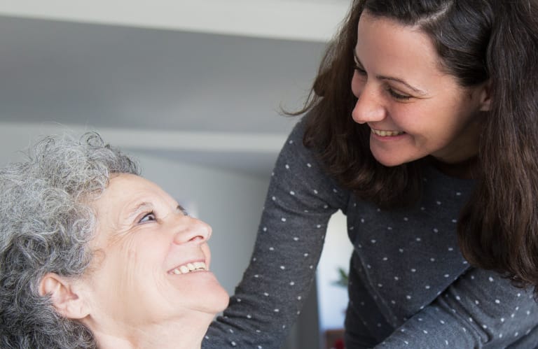 Eldery woman and her daughter looking each other in the eyes and smiling